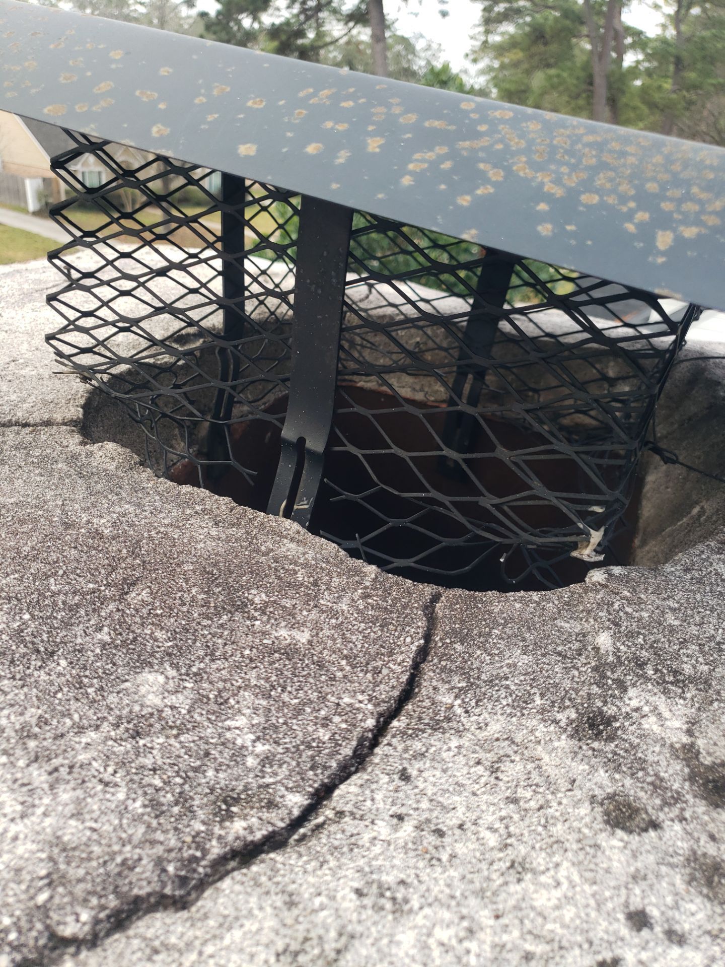 Cracked concrete around a dark opening covered by black netting and a metal grate-like barrier outdoors