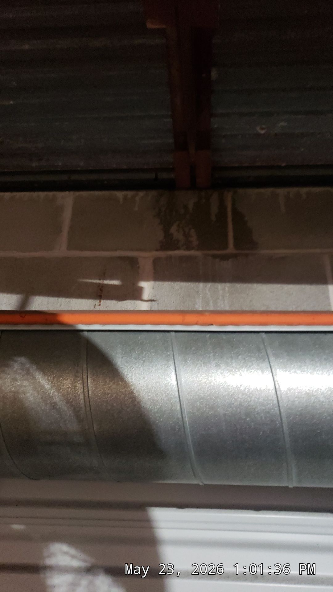 Industrial ceiling with dark metal beams, brown blocks, and a large silver duct pipe below.