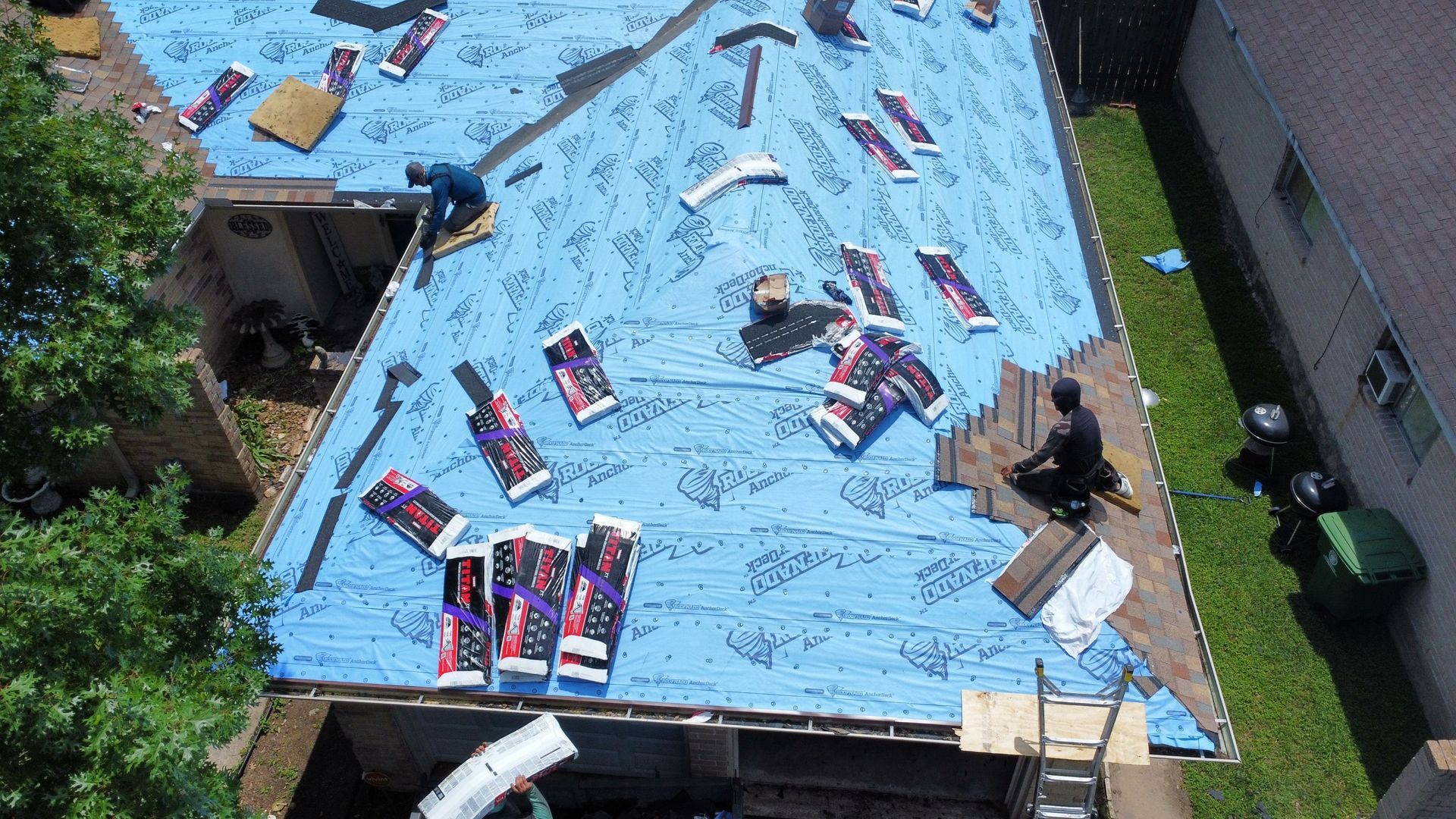 Rooftop covered in blue tarp with scattered red and blue packages, viewed from above.