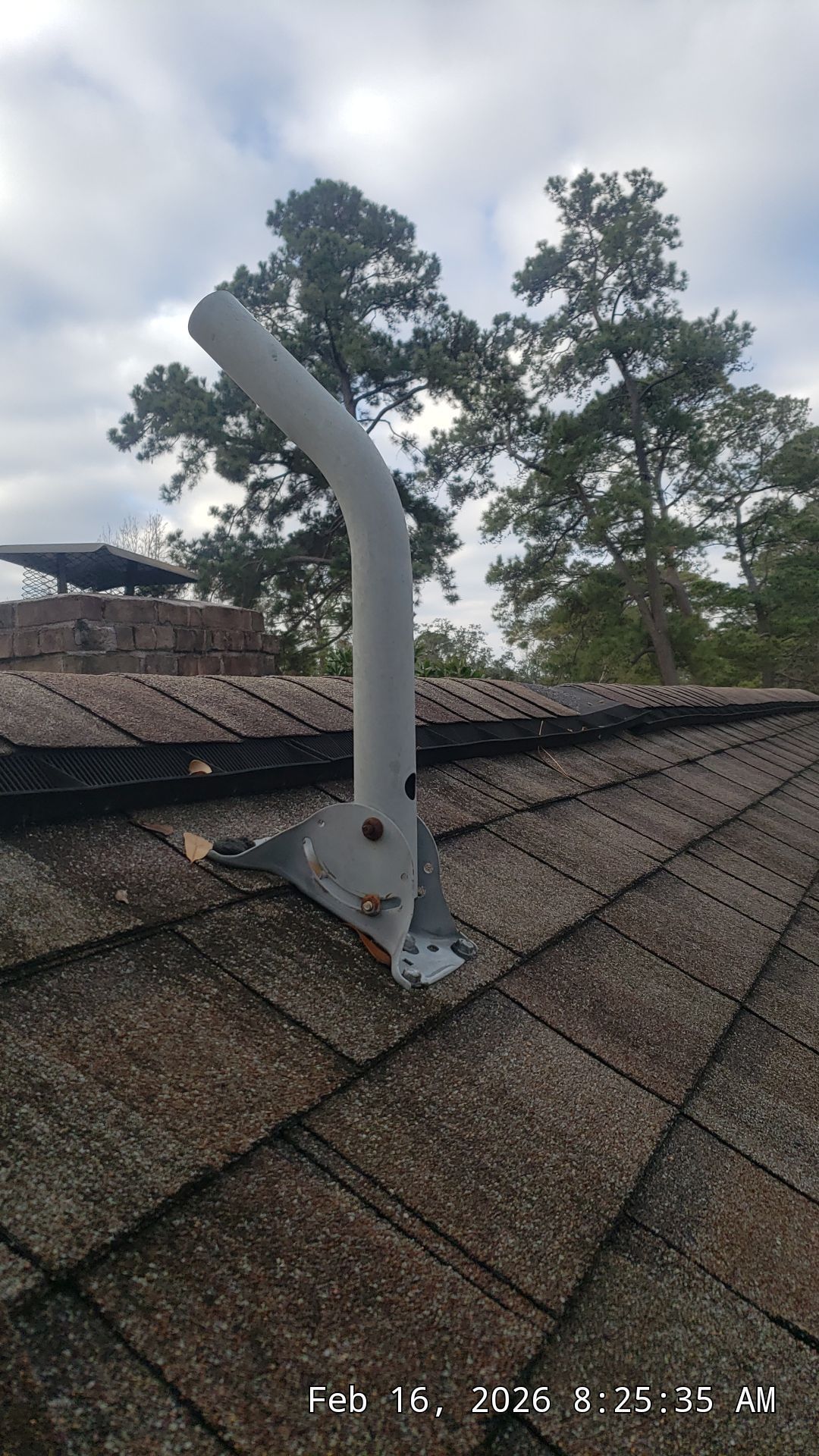 Roof vent pipe on a shingled rooftop with trees and cloudy sky in the background