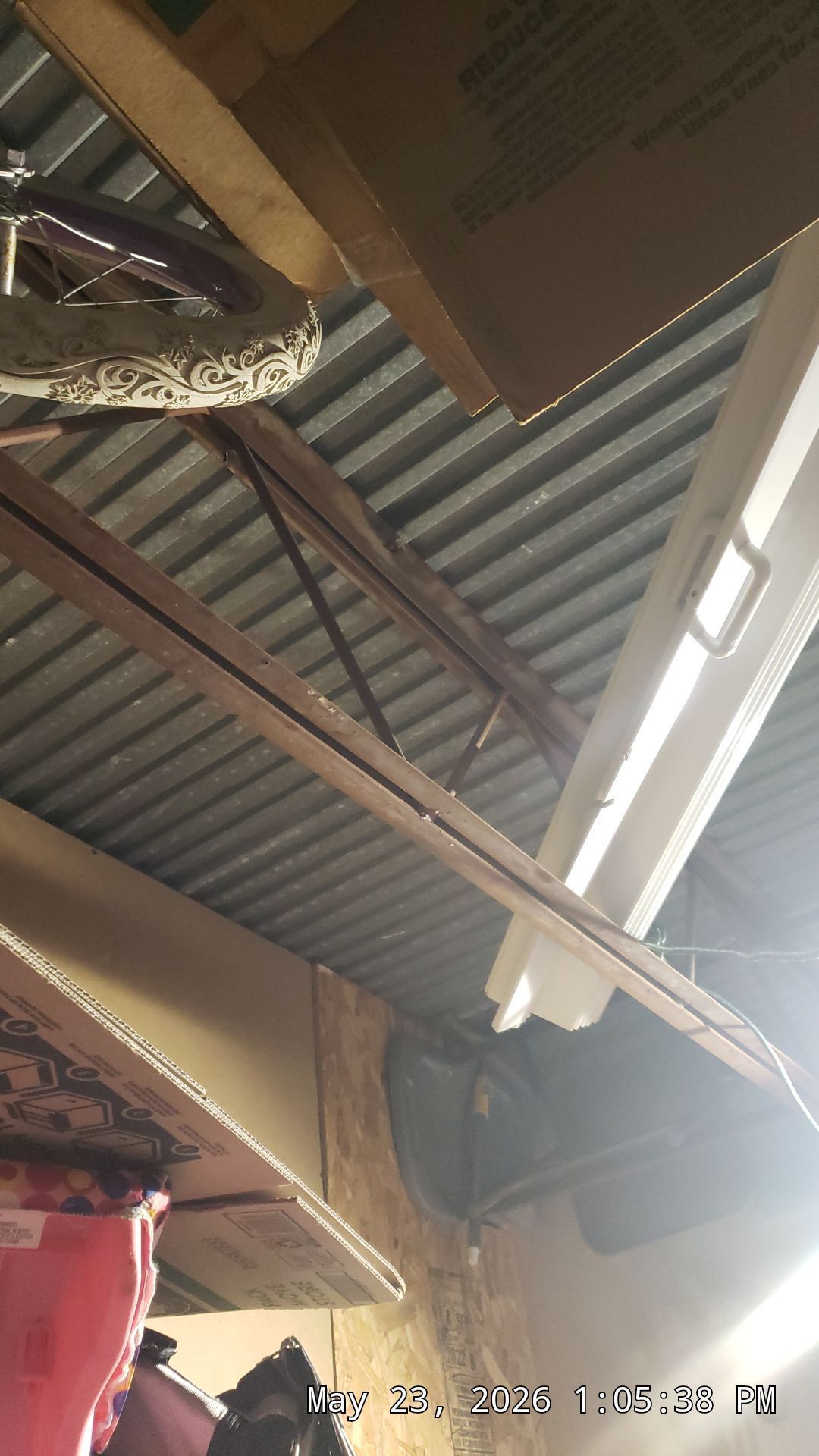 Corrugated metal ceiling with exposed beams, hanging ducting, and a ceiling light in a small industrial space