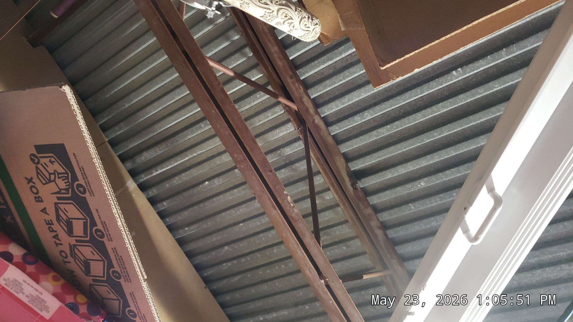 Corrugated metal roof with wooden beams and a cardboard sign hanging indoors