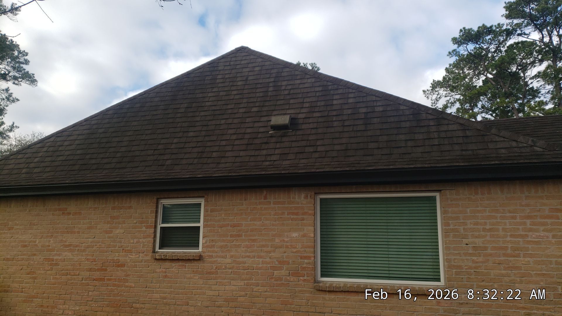 Brick house with dark shingled roof, small window, and green garage door under a cloudy sky