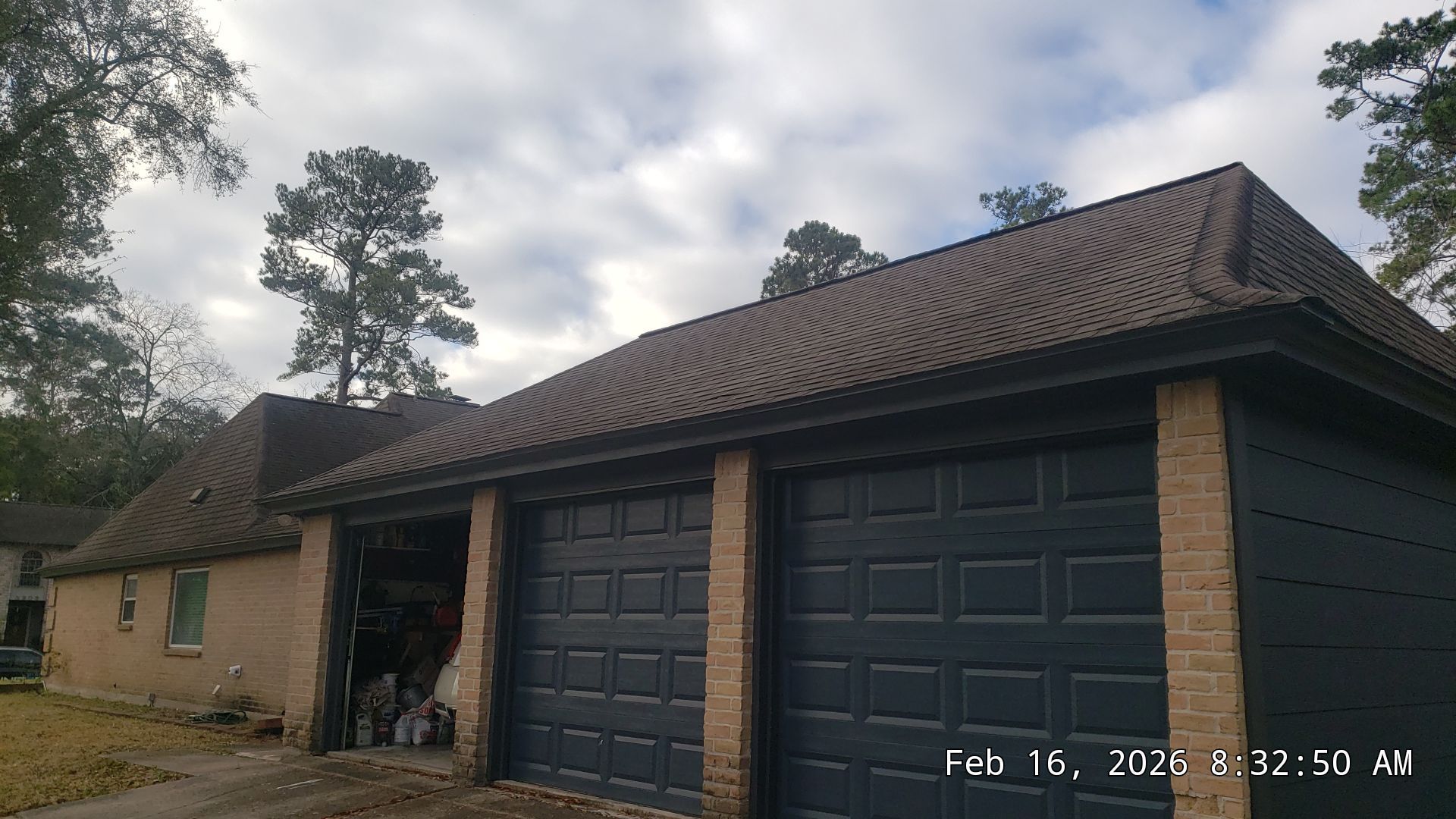 Suburban house with three dark garage doors, brick exterior, and a tall tree in the yard