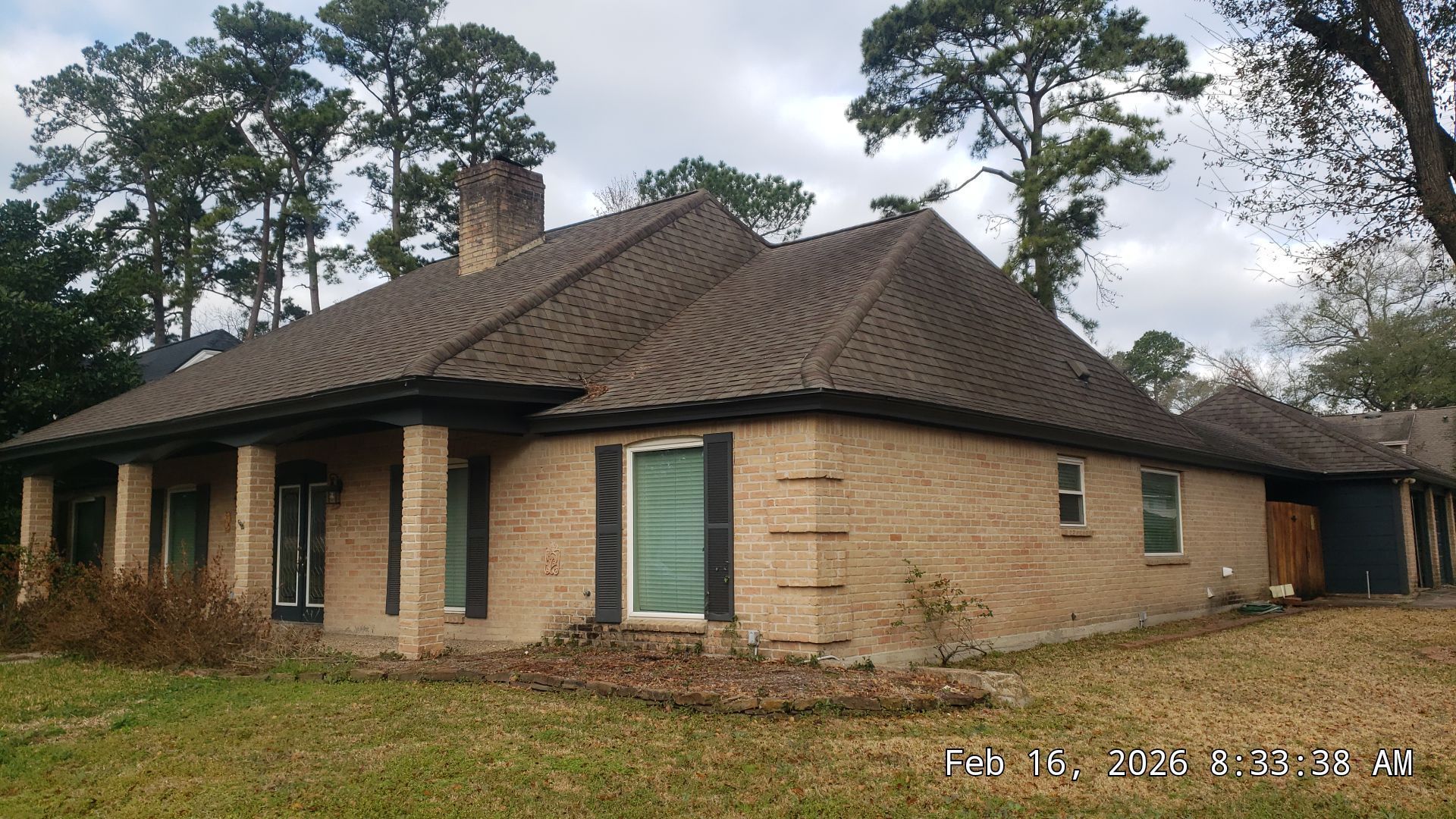 Single-story brick house with a dark roof and green shutters, surrounded by trees.