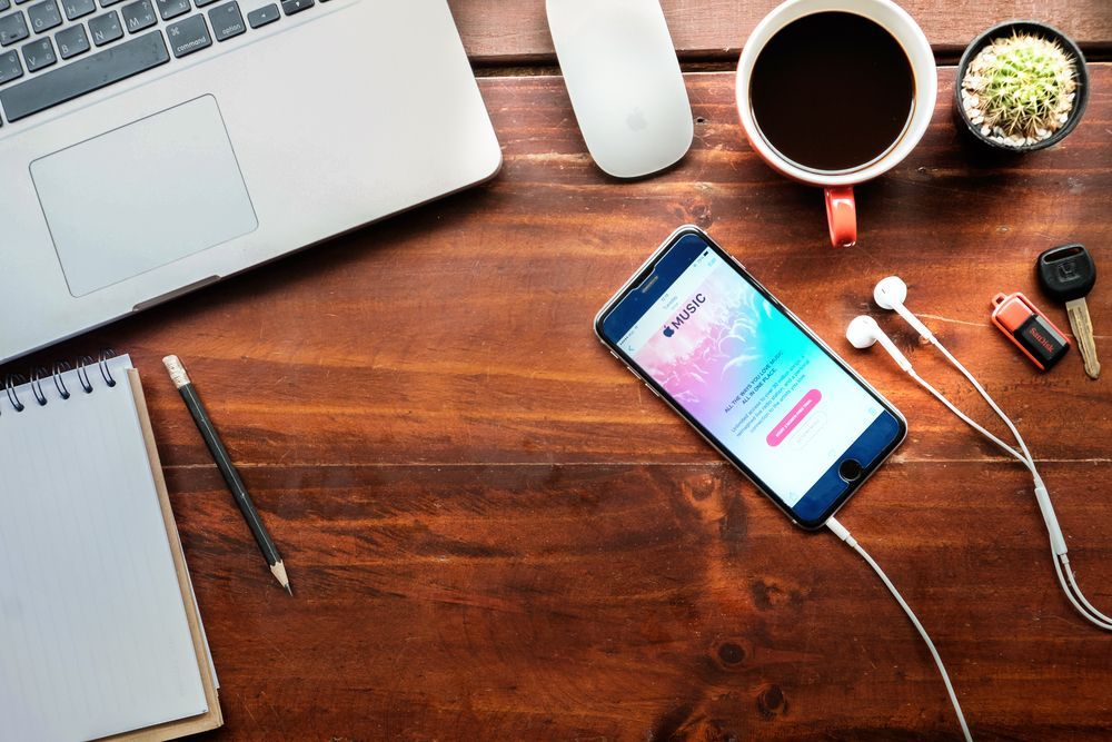 A cell phone is sitting on a wooden table next to a laptop and a cup of coffee.