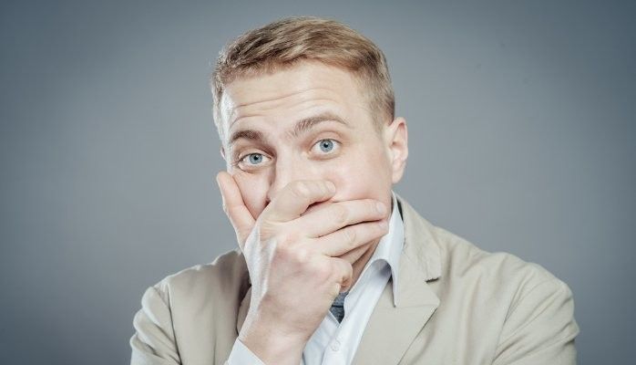 A man in a suit is covering his mouth with his hand.