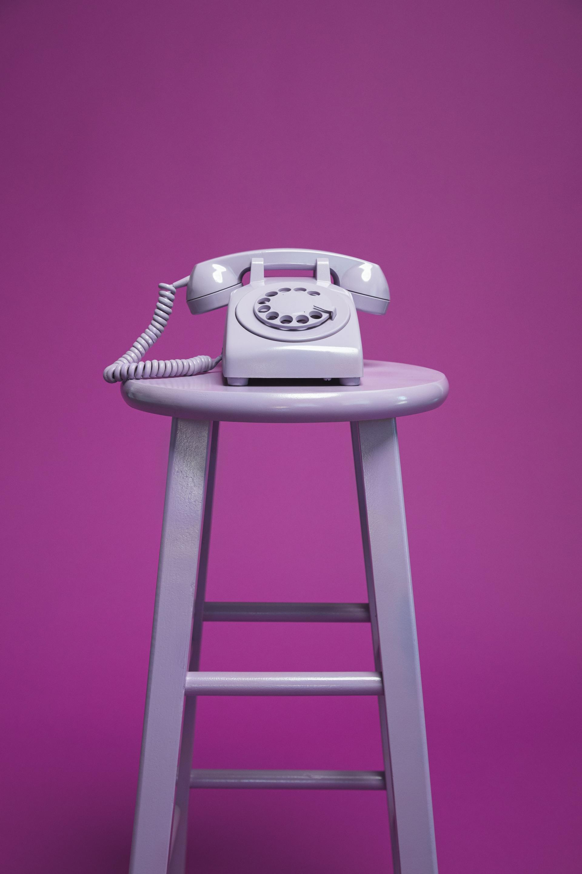 A white telephone is sitting on top of a purple stool.