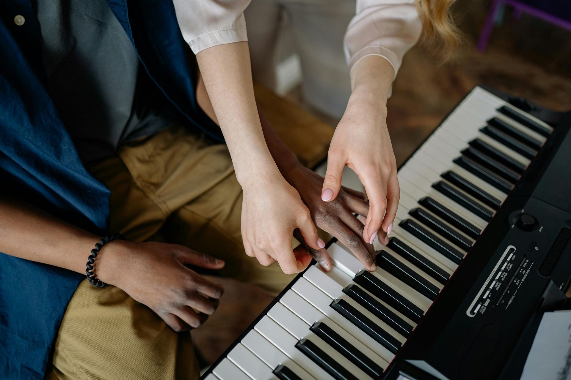 Two people playing a piano together, hands over black and white keys.