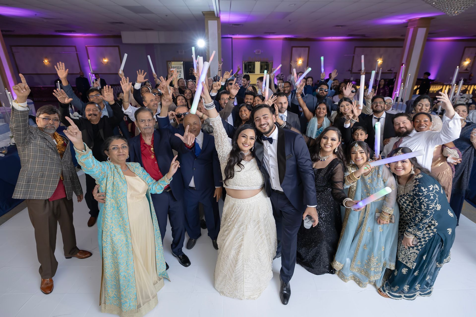Large group of people celebrating at an event, many holding glow sticks and smiling, indoors with decorations.