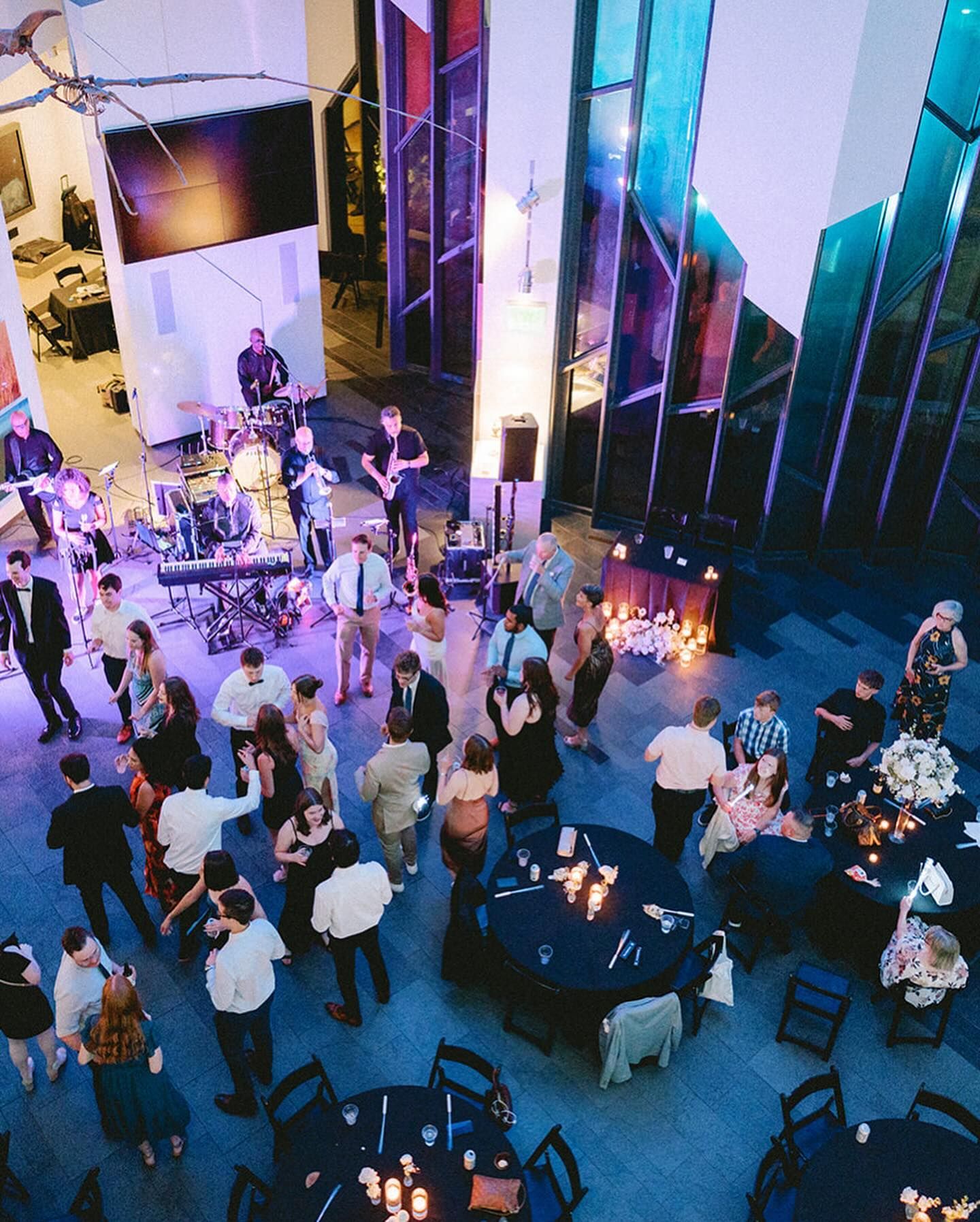 Wedding reception with dancing guests, band playing, and tables with candles in a venue with colorful stained glass.