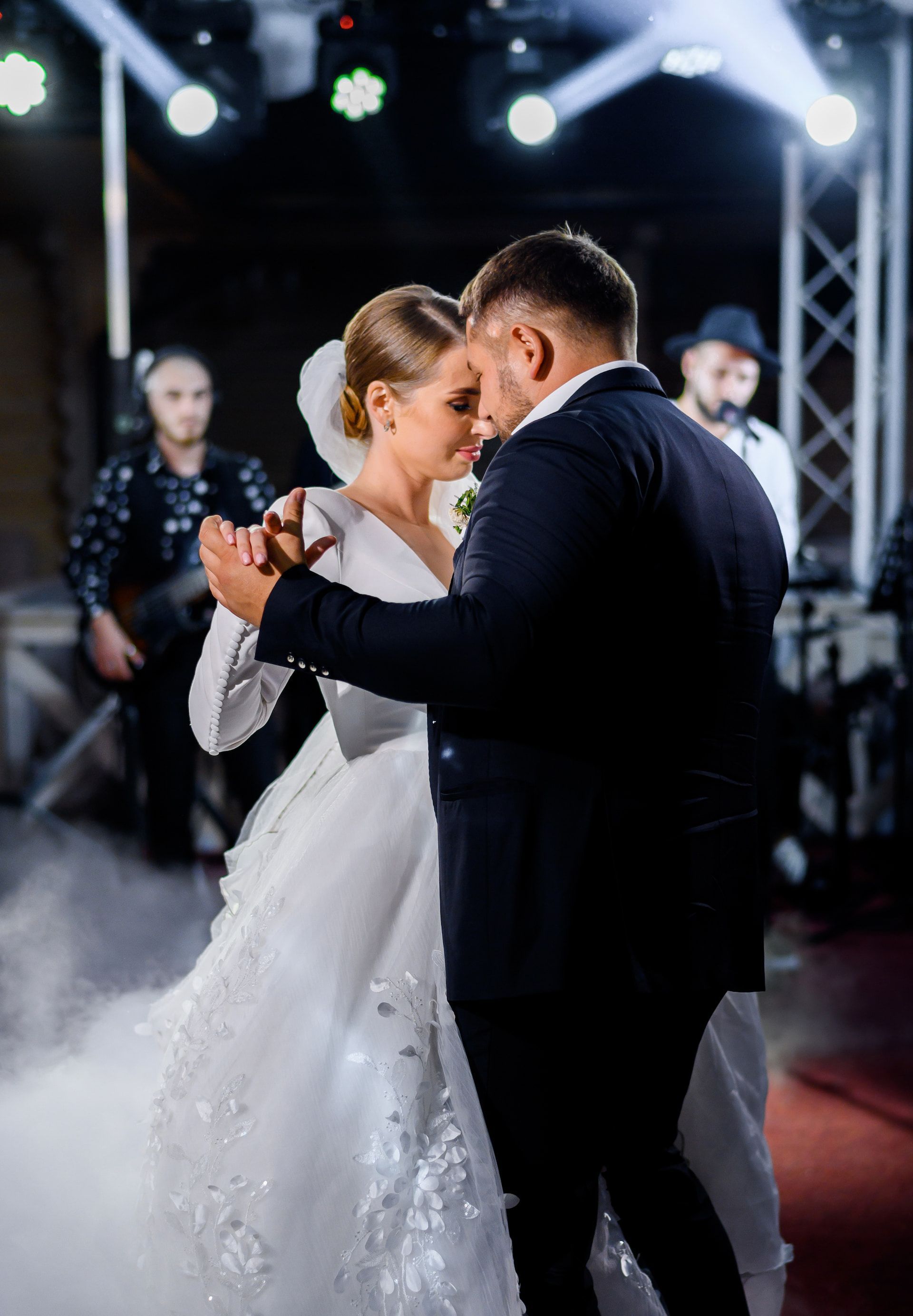 Bride and groom dancing at wedding reception. Smoke, band members, and stage lights in background.