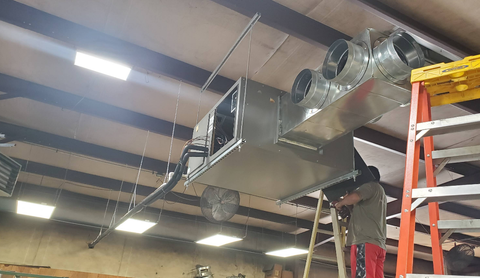 HVAC ductwork installation in a building. A person on a ladder works on hanging metal ductwork.