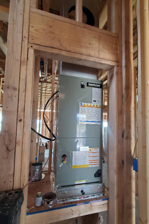 HVAC unit installed in a wooden frame during construction. Gray metal unit with warning labels.