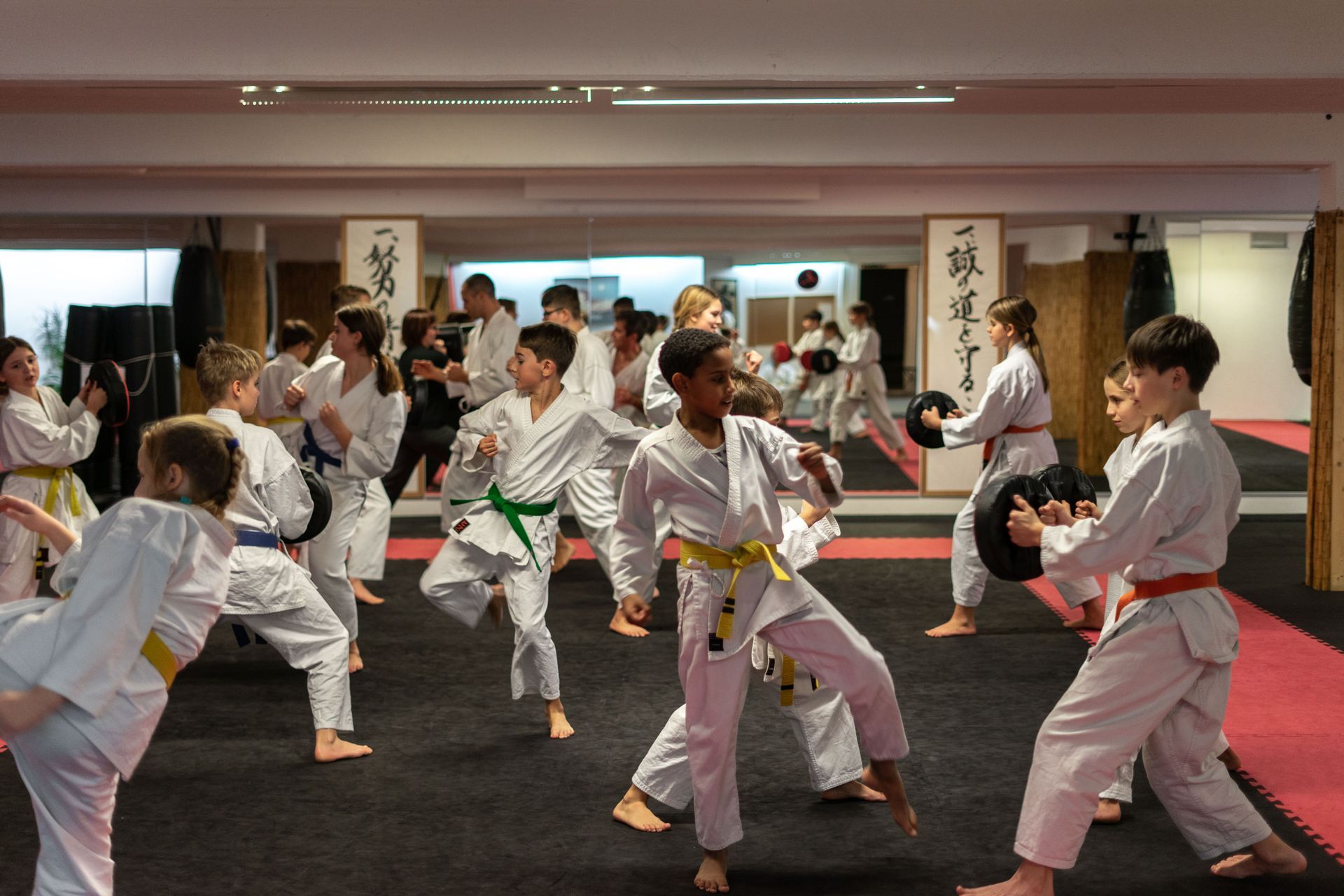 Kinder im Karatetraining führen Roundhouse-Kicks auf Schlagpolster aus.