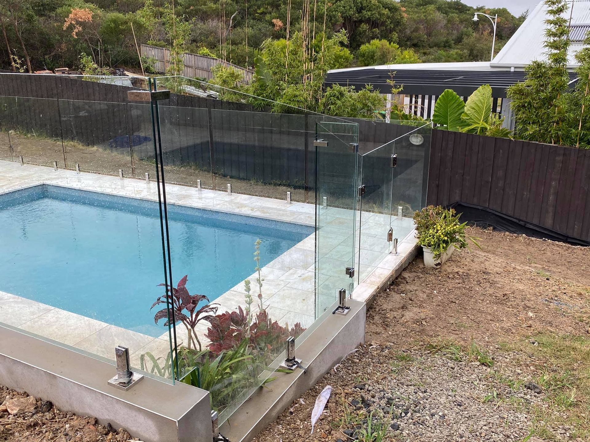 Glass Pool Fence Around a Pool, Surrounded by Plants and A Wooden Fence — Master Glass & Glazing in Belmont, NSW