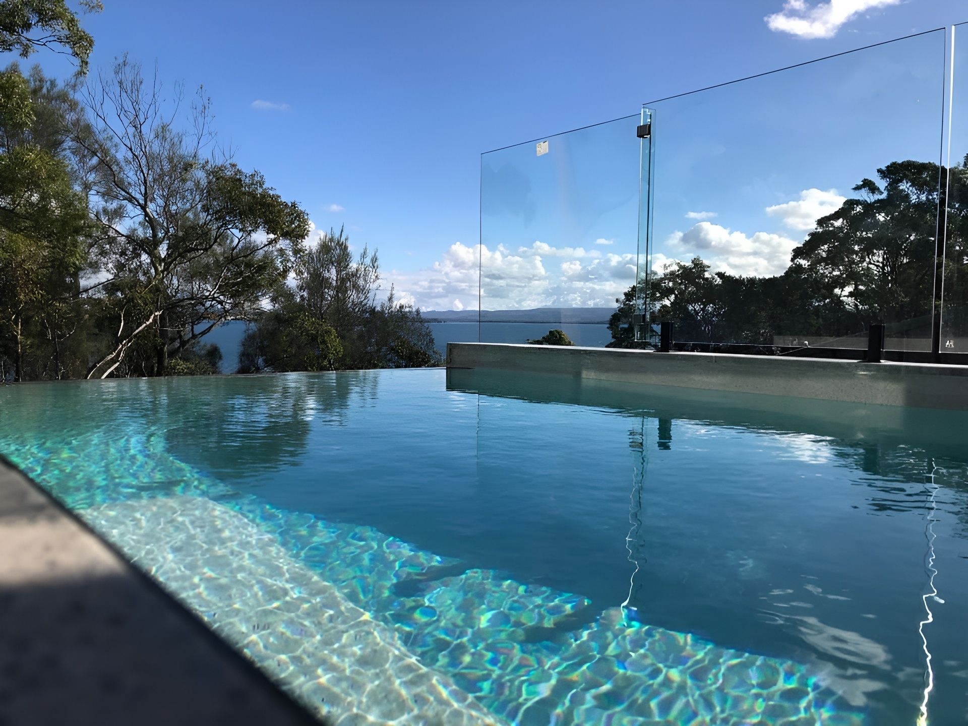 Infinity Pool Overlooking a Body of Water and Trees, Clear Glass Fence — Master Glass & Glazing in Maitland, NSW