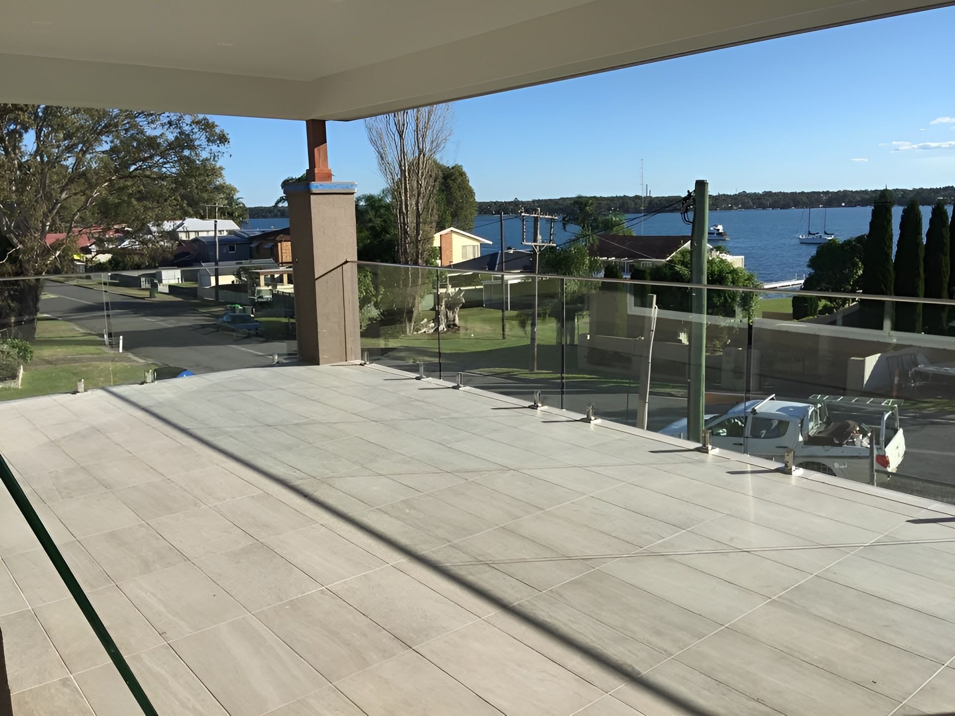 A Balcony with Glass Railings Overlooks a Waterway and Residential Area — Master Glass & Glazing in Merewether, NSW