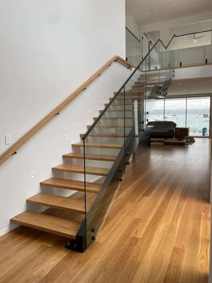 Wooden staircase with glass railing and handrail, leading up to a second floor.