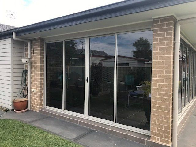 Sliding Glass Doors with Reflective Tint on A Brick and Stucco Building — Master Glass & Glazing in Newcastle, NSW