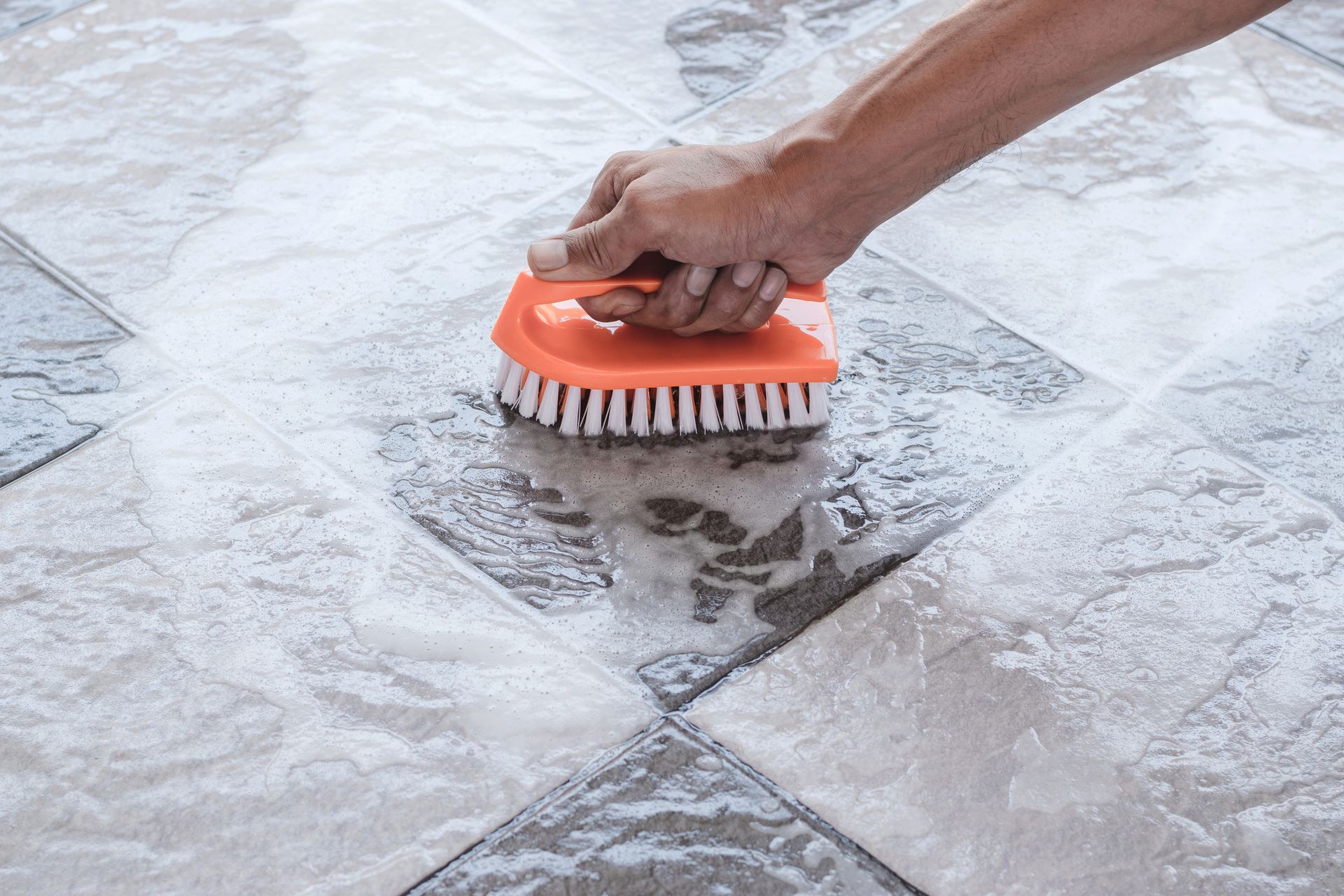 A person is cleaning a tile floor with a brush.