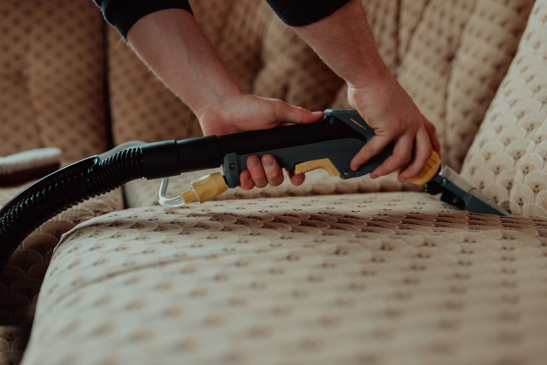 A person is cleaning a pattern couch with a vacuum cleaner.