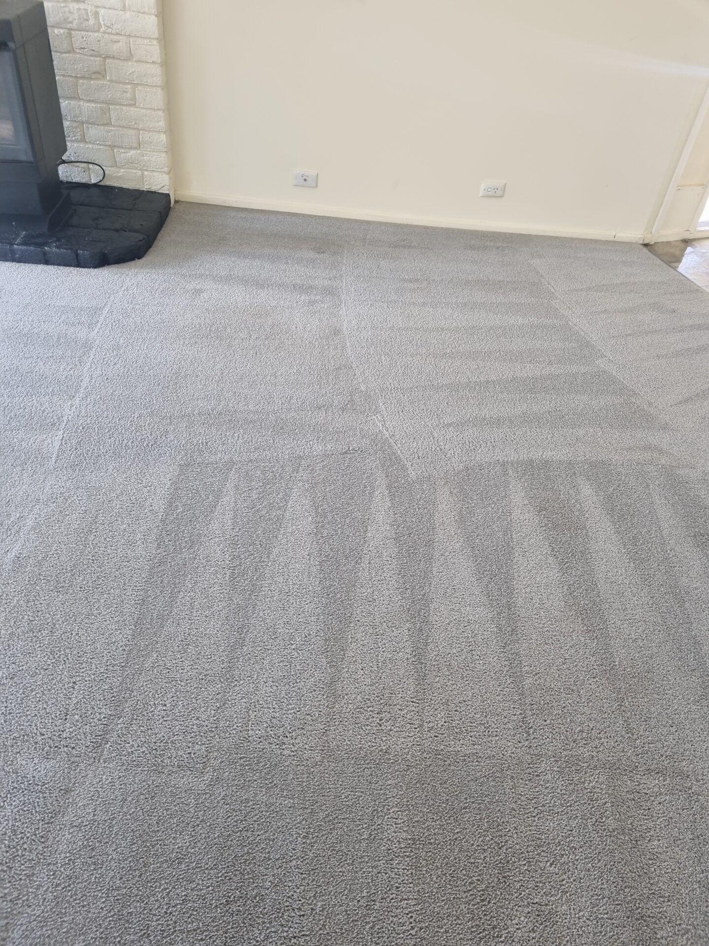 A living room with a clean gray carpet and a fireplace.
