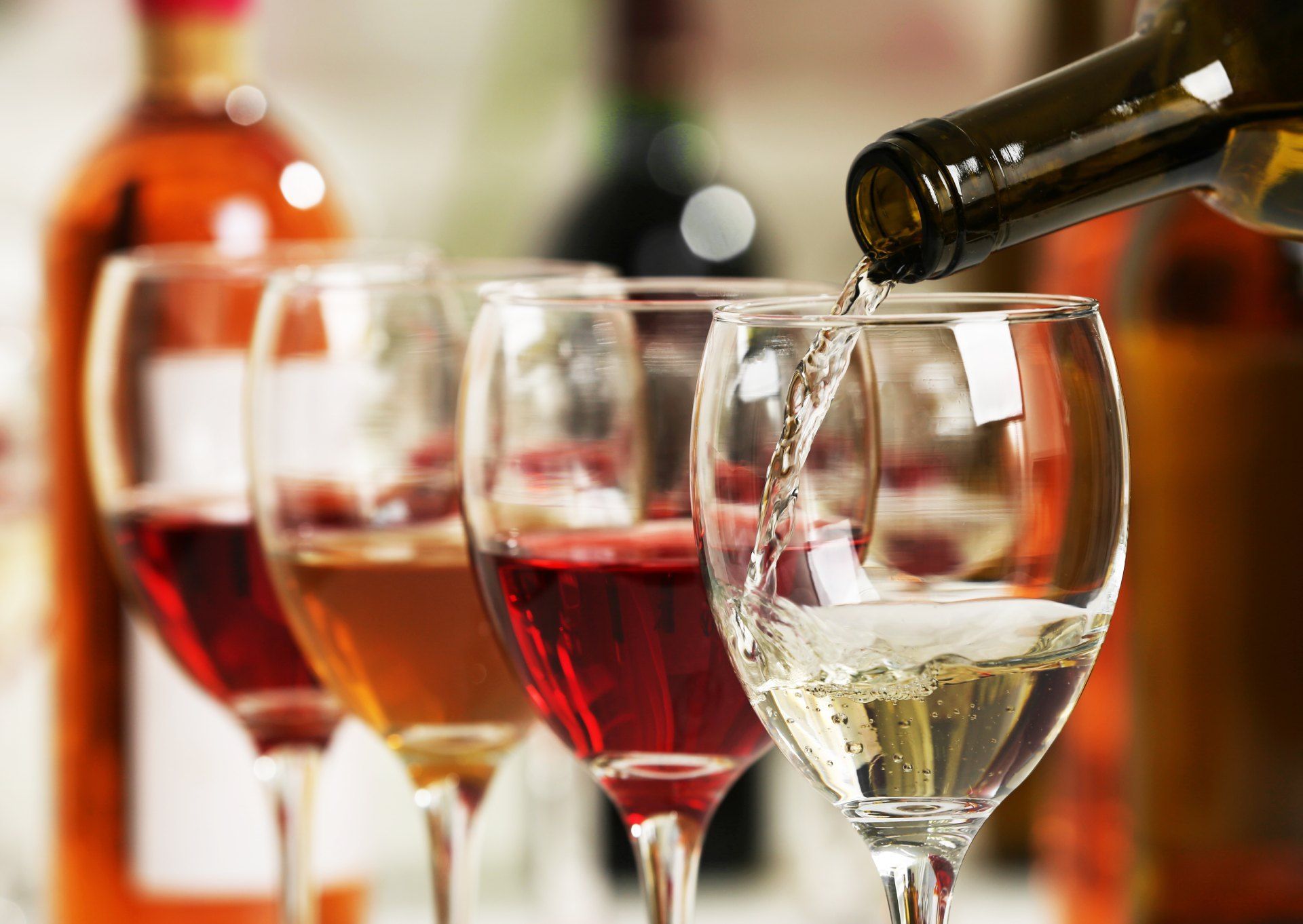 A bottle of wine is being poured into a row of wine glasses.