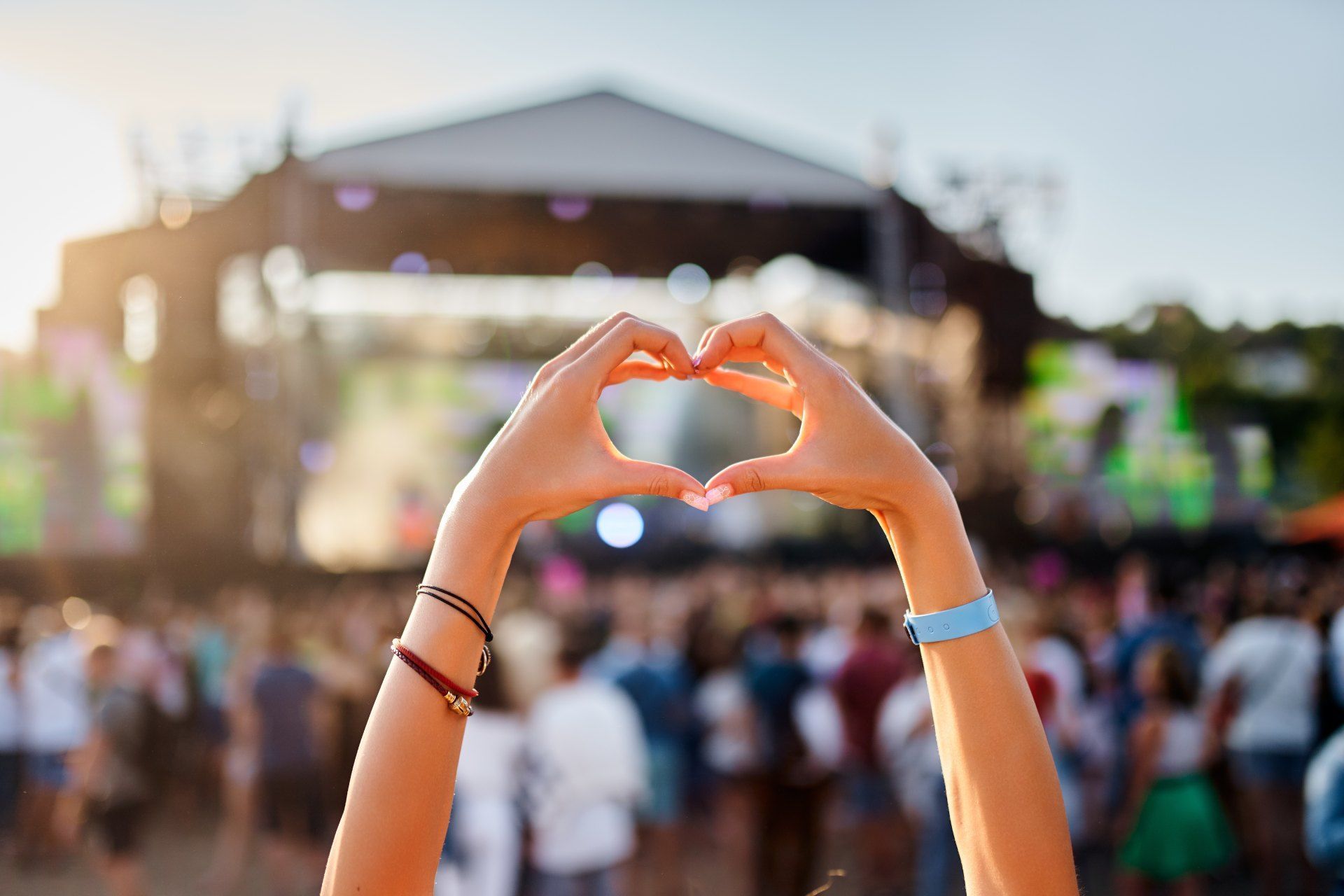 A woman is making a heart shape with her hands at a music festival.