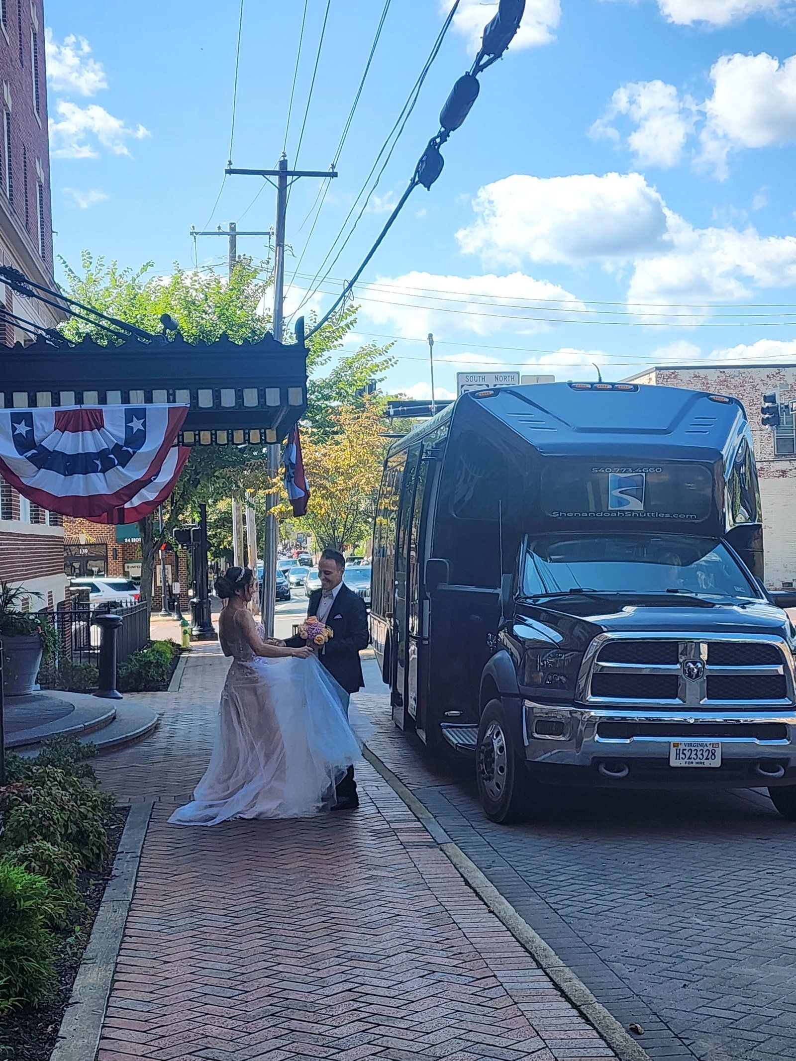 A bride and groom are standing on a sidewalk next to a bus.