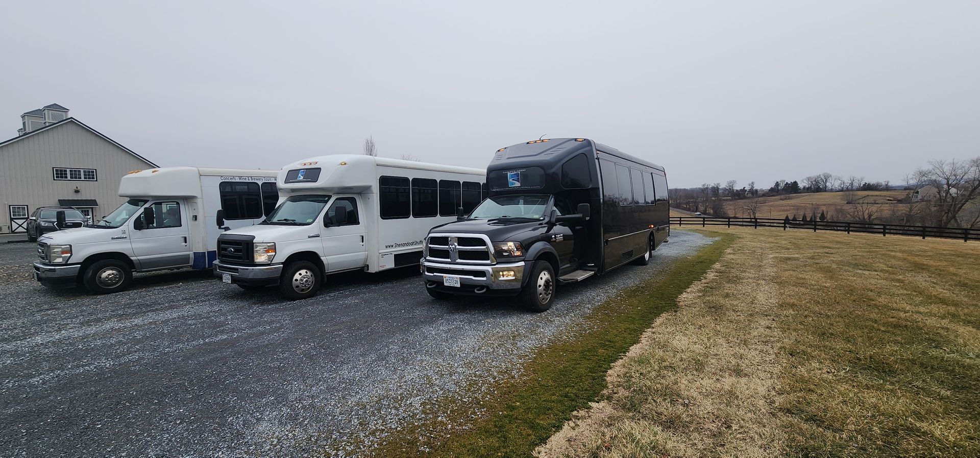 A row of buses are parked next to each other in a gravel lot.