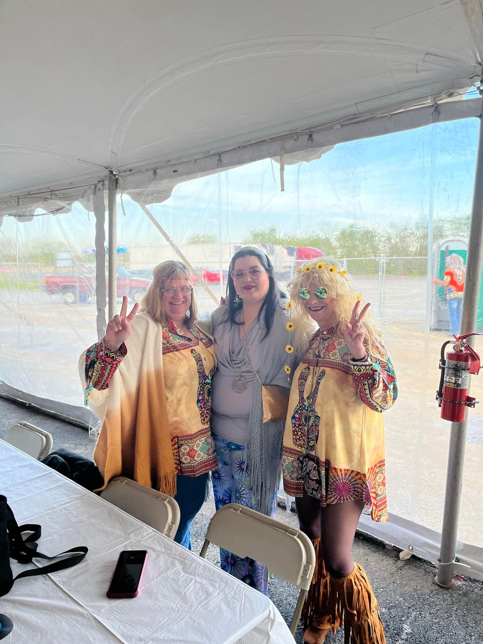 Three women are posing for a picture under a tent.