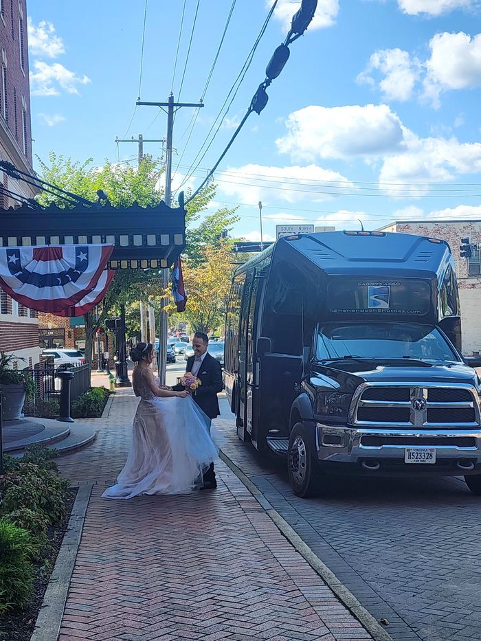 A bride and groom are standing on a sidewalk next to a bus.