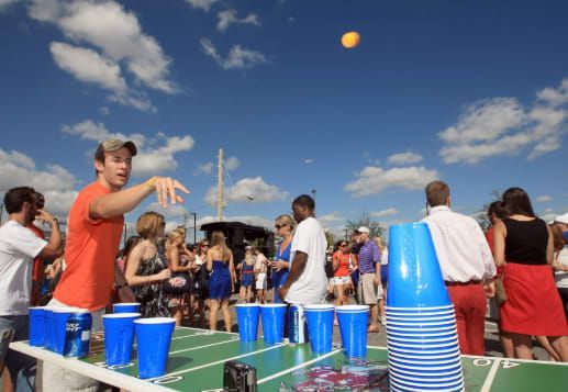 A group of people are playing beer pong with blue cups
