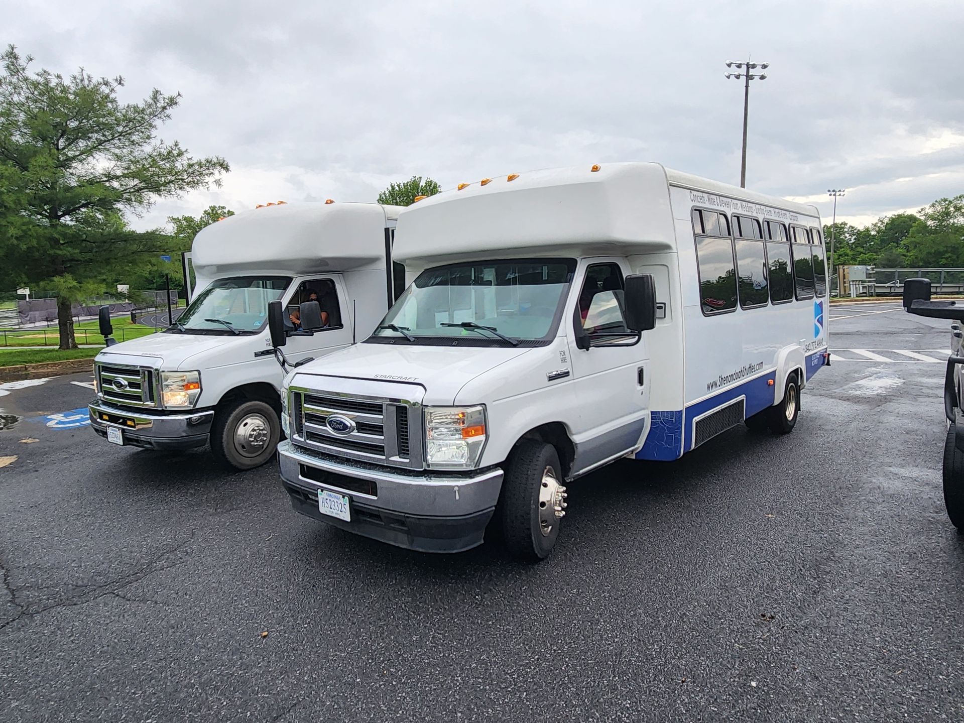 Two white buses are parked next to each other in a parking lot.