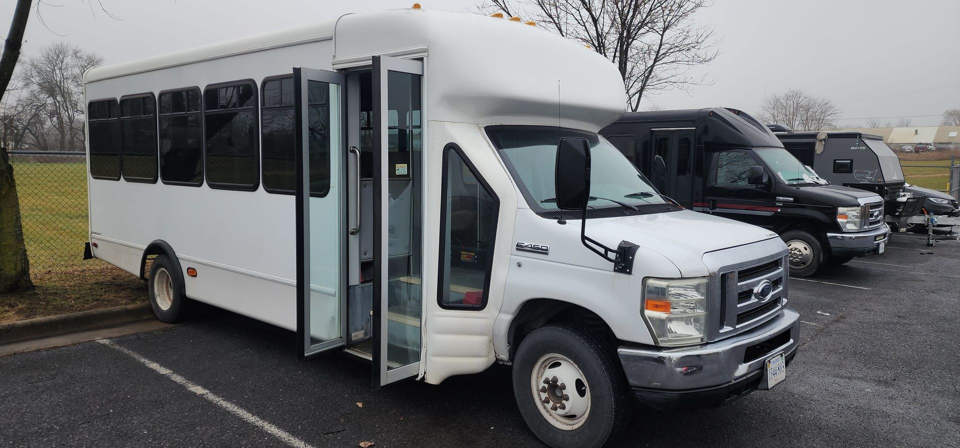 A row of white buses are parked in a parking lot.