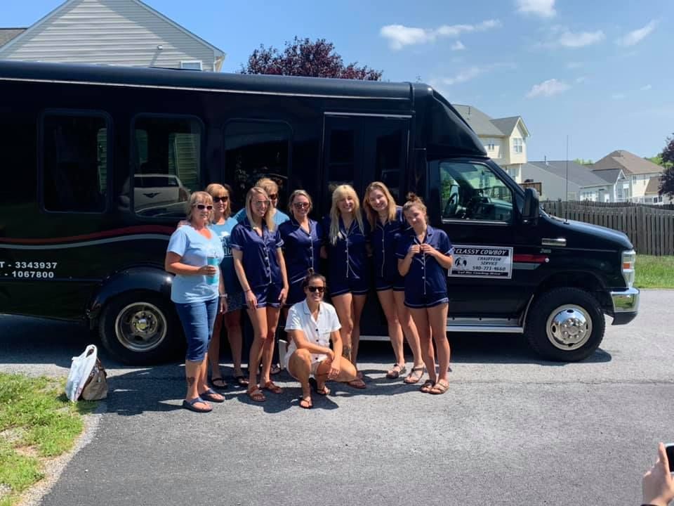 A group of women are posing for a picture in front of a black van.