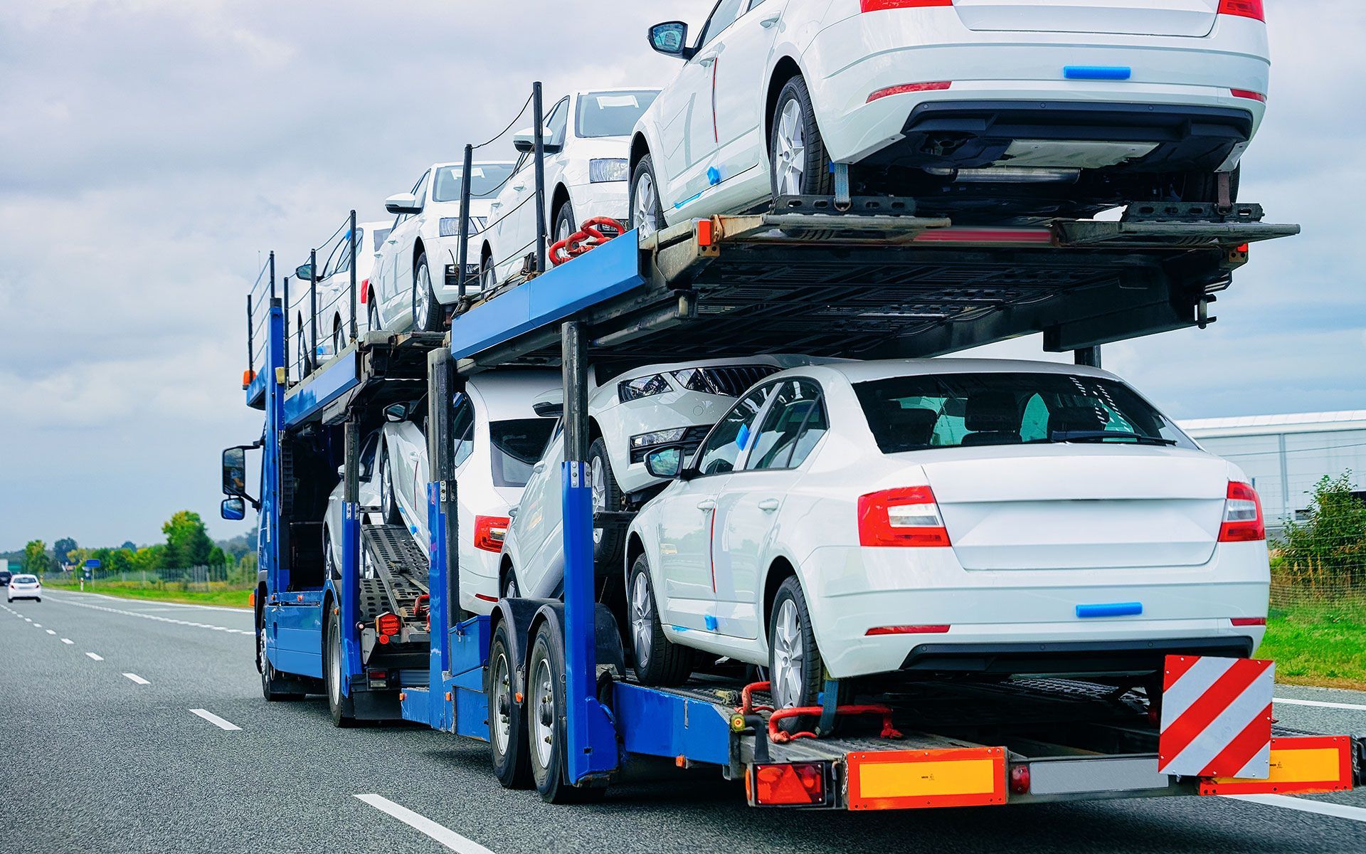 Car carrier truck transporting several white sedans on a highway.