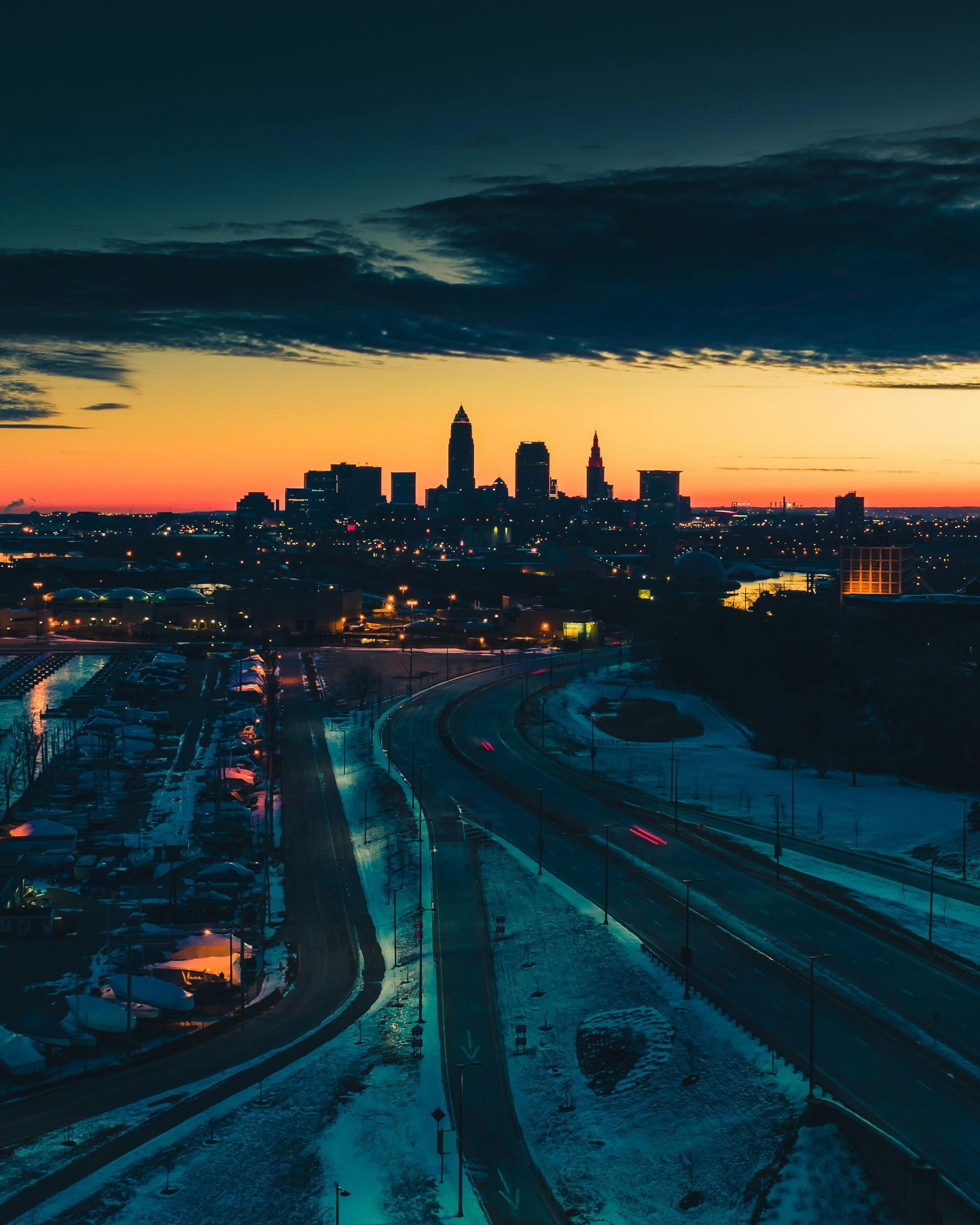 City skyline at sunset with a snow-covered foreground and a road leading towards the buildings.