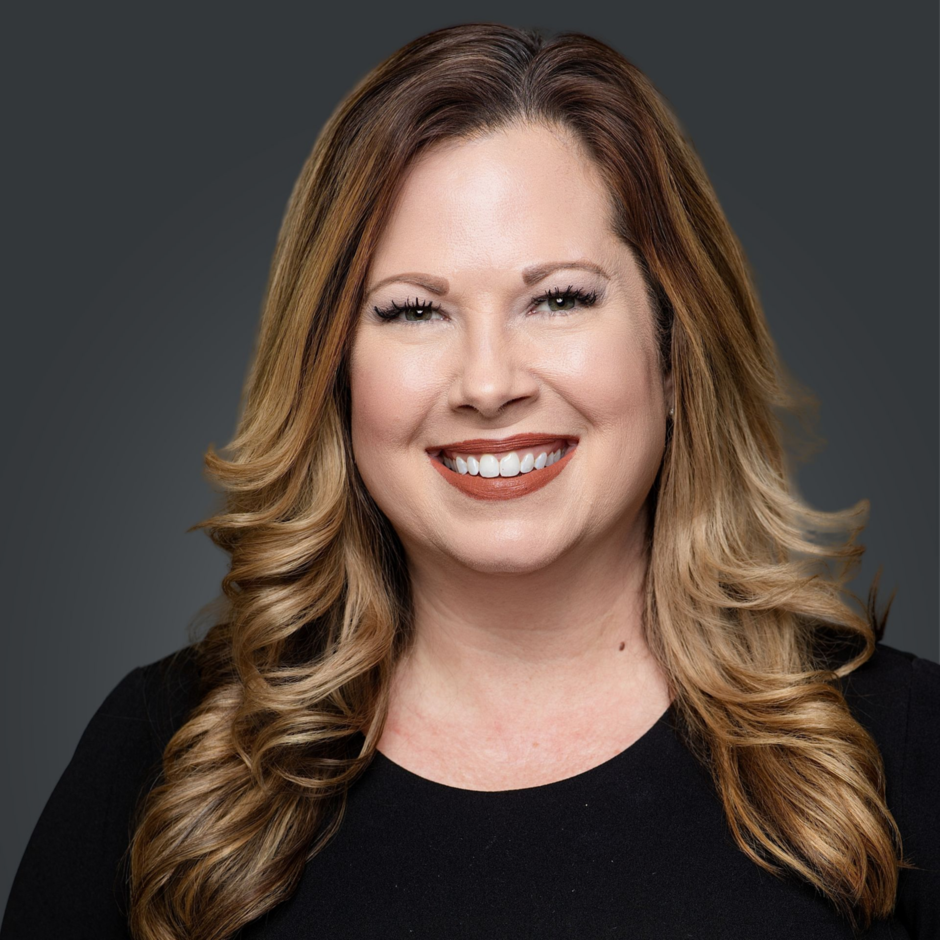 Woman with shoulder-length brown hair smiling, wearing a black shirt and red lipstick.