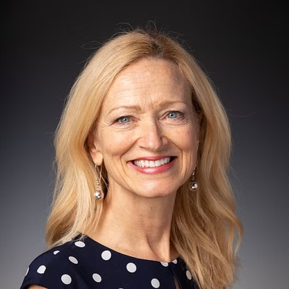 Woman with blonde hair smiles, wearing a navy polka dot dress and silver earrings.
