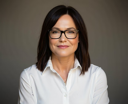 Woman with short dark hair, wearing glasses and a white button-down shirt, smiles at the camera. Neutral background.