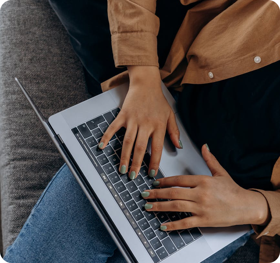 Person's hands typing on a laptop, wearing green nail polish, resting on their lap.