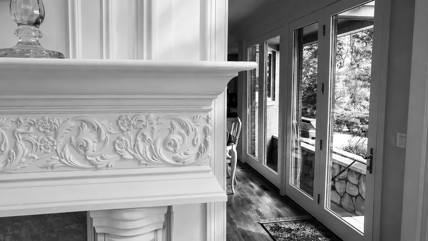Decorative white fireplace mantel in a bright room with tall windows and patterned curtains