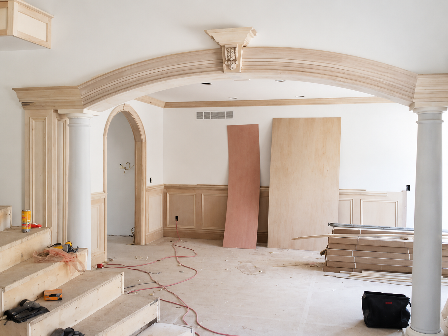 Unfinished room with ornate arched trim, wood paneling, tools, and materials on the floor
