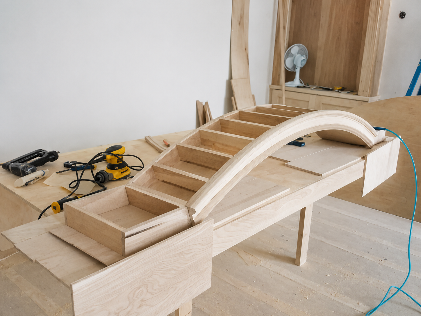 Wooden model bridge with arched deck and steps, on a workshop table with tools nearby
