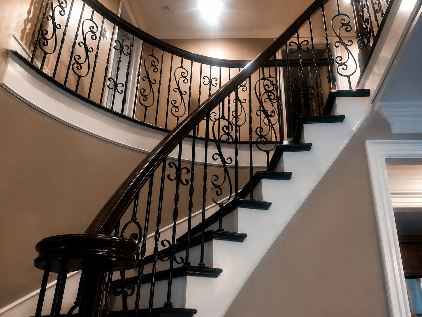 Curved staircase with black wrought-iron railing in a warmly lit interior foyer