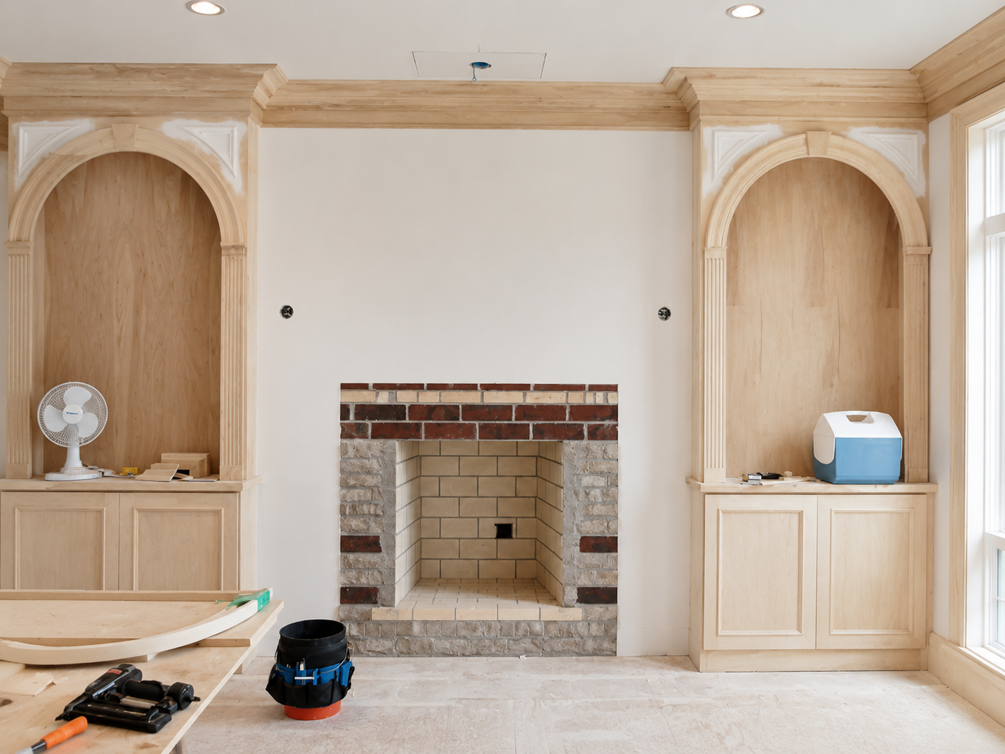 Built-in cabinets flanking a white fireplace surround in a light wood room under construction