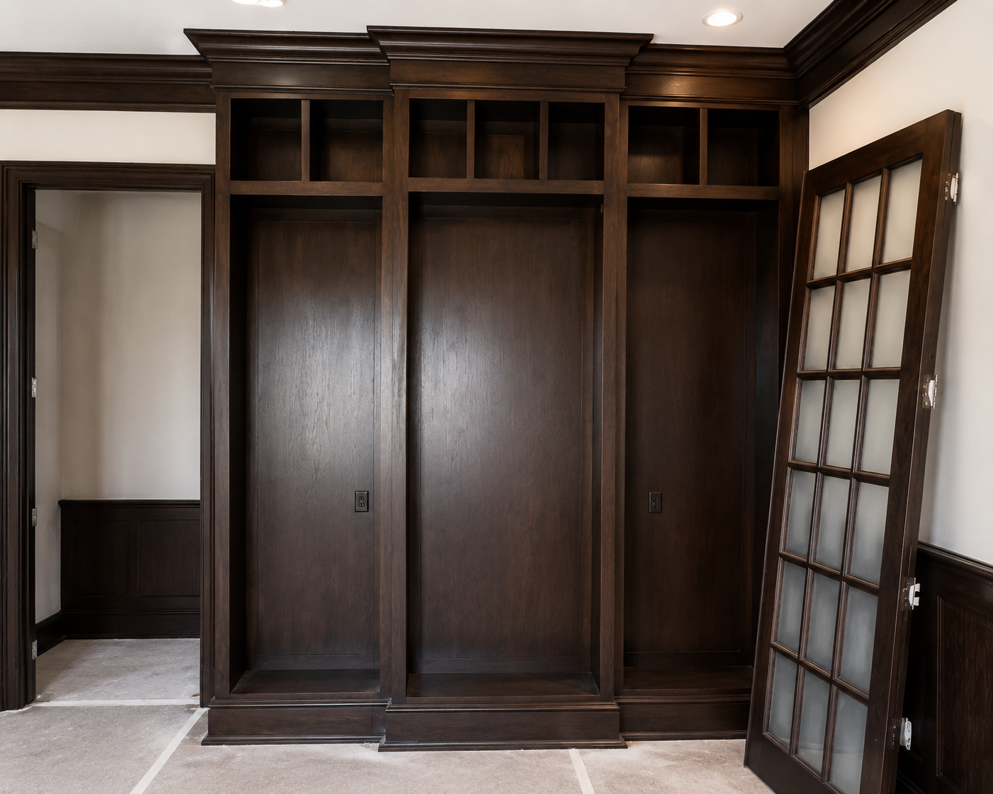 Dark wood built-in wardrobe with cabinets and open shelving in a room, beside a paneled glass door.
