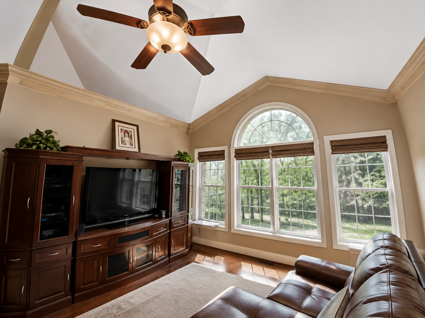 Bright living room with arched window, wood entertainment center, leather sofa, and ceiling fan